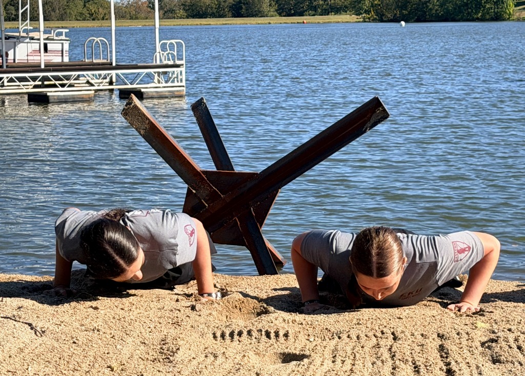 EKU ROTC Cadets doing 4-count pushups in the sand directly facing forged steel Czech hedgehogs at Queenslake
