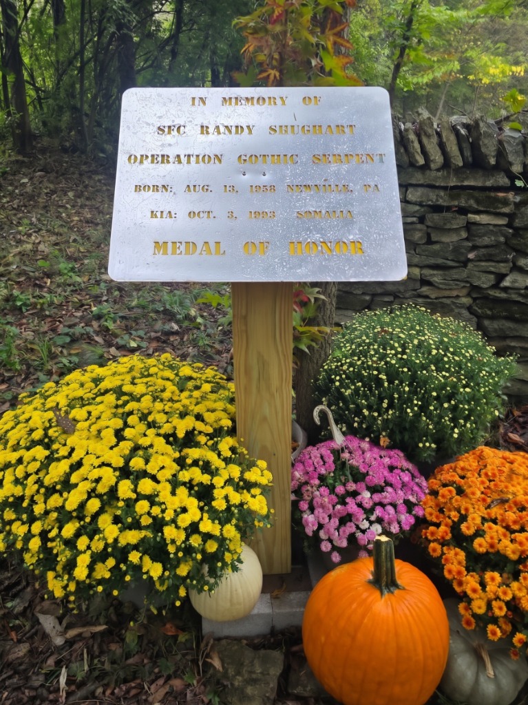 SFC Randy Shughart Medal of Honor Memorial Wall Plaque surrounded by vibrant autumn mums and pumpkins at Queenslake